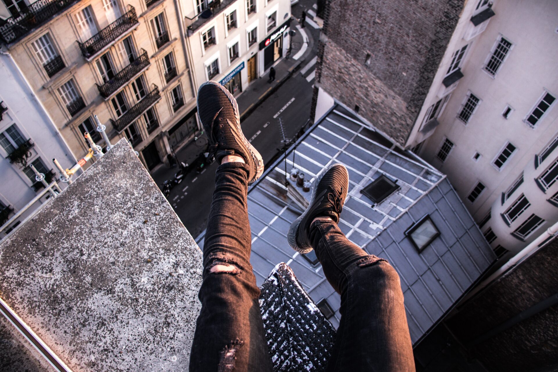 Nogi mężczyzny siedzącego na dachu wieżowca